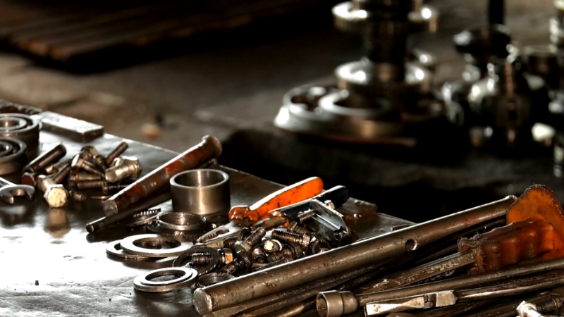 A variety of industrial spare parts, including bolts, bearings, and tools, arranged on a workbench in a workshop